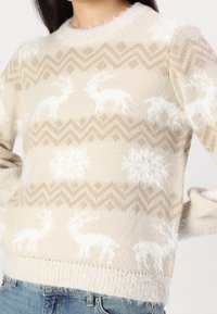 Maglione lavorato a maglia beige con motivi bianchi di animali e fiocchi di neve, con una finitura testurizzata e bordi sfrangiati nel colletto e nell'orlo.