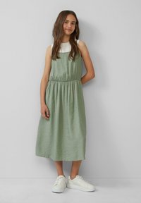 Grünes Midikleid aus leichtem Stoff, mit einem elastischen Taillengummi und einem entspannten Schnitt, kombiniert mit weißen Sneakers.