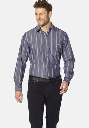 Marineblaues Hemd mit Knöpfen und vertikalen weißen Streifen, langen Ärmeln und einer linken Brusttasche. Kombiniert mit schwarzen Jeans und einem schwarzen Gürtel.