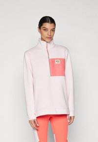 Pulover roz deschis cu guler înalt, fermoar până la jumătate și buzunar corai. Țesătură moale, dotat cu patch cu logo și manșete cu riburi. Asortat cu pantaloni corespunzători.