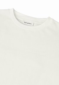 Bílý bavlněný tričko s kulatým výstřihem a štítkem s nápisem "OH APRIL" uvnitř. Hladká textura, standardní design s krátkým rukávem.
