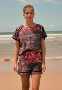 Geprinte twee-delige outfit met een kortemouwen top en shorts in tinten roze, paars en donkerblauw, met gegolfde randen en complexe patronen.
