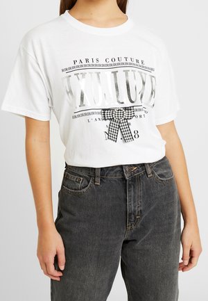 Witte T-shirt met zilveren tekst "EXULUXE", zwarte Paris Couture-print en een zwart-wit houndstooth strik, gecombineerd met donkergrijze jeans.