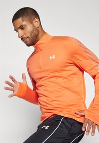 Orange athletic top with a quarter-zip design, made from smooth fabric. Features textured accents on shoulders and a logo on the chest. Black pants.