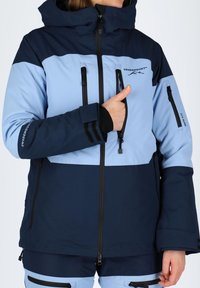 Niebieska i granatowa kurtka śniegowa z kapturem, wyposażona w wiele zamykanych na zamek kieszeni, regulowane mankiety oraz logo górskie. Miękka tekstura, sportowy design.