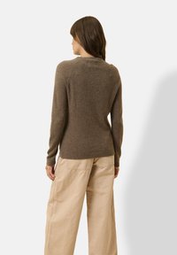 Maglione marrone in lana con scollo a costine e maniche lunghe. Il materiale sembra morbido con una finitura testurizzata. Abbinato a pantaloni beige a gamba larga.