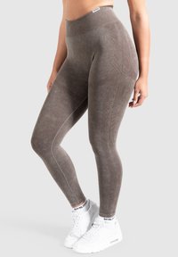 Leggings marroni con texture, dotati di una vita alta, con dettagli a coste e design aderente. Indossati con sneakers bianche.