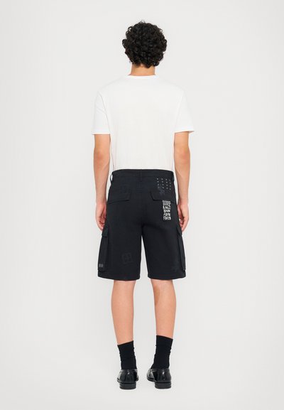 Schwarze Cargo-Shorts mit mehreren Taschen und dezenten strukturierten Mustern. Kombiniert mit einem schlichten weißen T-Shirt mit kurzen Ärmeln.
