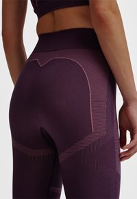 Paarse sportleggings met textuurpatronen en een hoge tailleband. Voorzien van een uitsnijding aan de achterkant en contrasterende roze lijnen.