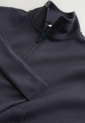 Marineblauer Fleecepullover mit Reißverschluss, hohem Kragen, glatter Textur und schwarzem Reißverschluss. Das Design umfasst lange Ärmel und eine flache Nahtverarbeitung.