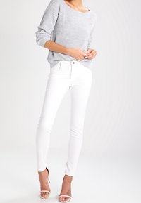 Šedý žebrovaný svetr s uvolněným střihem, spárovaný s bílými skinny džíny, které mají hladkou texturu a klasický pětikapsový design.