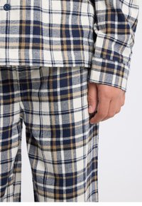 Plaid pajama set in blue, cream, and tan colors. Soft cotton material, featuring a classic check pattern. Button-up shirt detail visible.