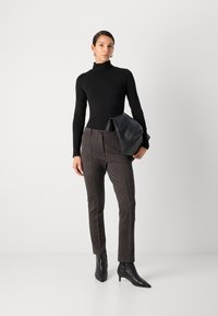 Haut à col roulé noir associé à un pantalon ajusté noir et blanc à pois, mis en valeur par des bottines à talons aiguilles noires et un sac en cuir noir.