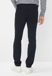 Marineblaue Slim-Fit-Hosen aus Stretchstoff mit Gesäßtaschen und Gürtelschlaufen. Dazu weiße Sneakers.