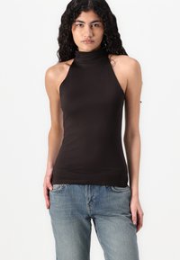 Top fără mâneci, de culoare maro, cu un design ajustat. Fabrică moale și elastică, cu margini fără cusături, purtat cu blugi din denim ușor albastru.