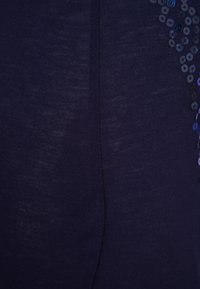 Top blu navy realizzato in un tessuto morbido e strutturato, con una fila di paillettes circolari lungo un lato per un dettaglio aggiuntivo e un interesse visivo.