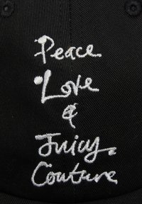 Zwarte pet met witte geborduurde tekst "Peace, Love & Juicy Couture." Kenmerkt zich door een gestructureerde vorm en textiel met een textuur.