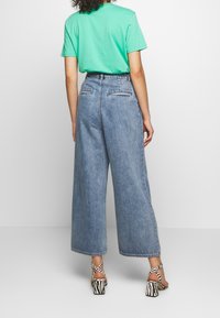 Vaaleansiniset, leveälahkeiset farkut, joissa on korkea vyötärö, takataskut ja raaka helma, yhdistettynä mintunvihreään T-paitaan ja kuvioituihin korkokenkiin.