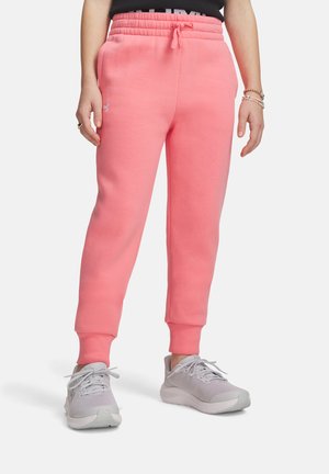 Personne portant un jogging rose à cordon avec des poignets côtelés et des chaussures de sport gris clair, debout les mains détendues.