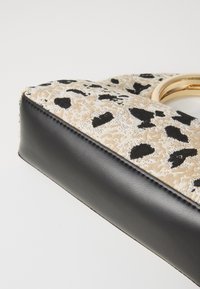 Handbag featuring a printed beige fabric with black leopard spots, complemented by a black leather base and a gold circular hardware accent.