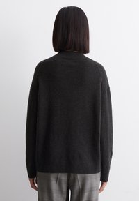 Pull en maille gris foncé avec un col montant, des épaules tombantes et un ourlet côtelé, associé à un pantalon à carreaux clair. Texture lisse.