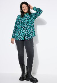 Langärmliges Hemd in Teal mit pinkem und schwarzem Leopardenmuster. Schwarze Skinny-Jeans und knöchelhohe schwarze Stiefel mit dicken Sohlen.