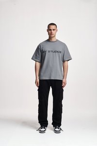 Tricou gri cu mânecă scurtă, având textul negru "2Y STUDIOS", asociat cu pantaloni cargo negri, care au multiple buzunare laterale, și adidași albi.