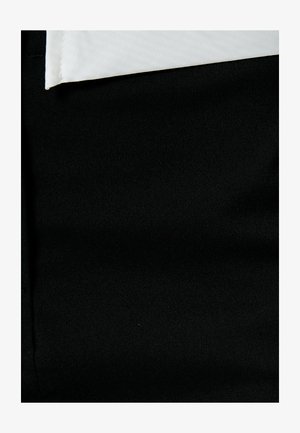 Schwarzer Stoff der Hose mit glatter Textur, darunter ein weißes Hemd, das am oberen Rand teilweise sichtbar ist.