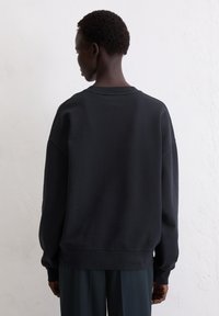 Zwarte sweatshirt met een ronde hals, verlaagde schouders en geribde mouwen. De stof lijkt zacht en soepel, met minimale stikseldetails.