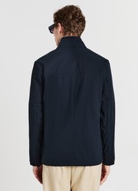 Giacca blu navy con collo alto e maniche lunghe. Tessuto liscio, design minimale e dettagli di cuciture sottili su spalle e maniche.