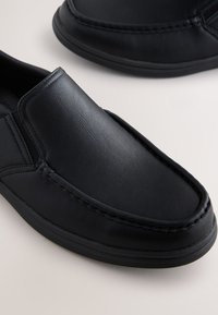 Chaussures noires à enfiler en cuir lisse, avec un bout arrondi, des accents cousus, et une semelle en caoutchouc à finition texturée.