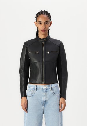 Veste en cuir noir courte avec épaules structurées, fermeture éclair à l'avant et poches sur la poitrine, associée à un jean en denim clair. Texture lisse, coupe ajustée.
