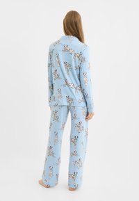 Hellblaues Pyjama-Set mit einem aufgedruckten Dalmatiner-Muster; Langarmoberteil und weit geschnittene Hosen aus weichem, glattem Stoff.