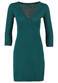 Robe en maille longueur genou couleur sarcelle, manches trois-quarts, col en V, avec un motif ajouré en forme de cœur sur les manches et le haut du buste.