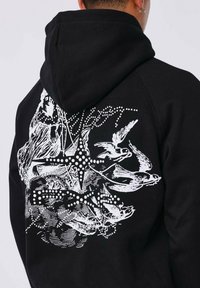 Zwarte hoodie met een witte grafische afbeelding van een persoon, vogels in de vlucht, en een stervormig patroon van stippen op de achterkant.