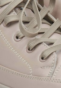 Light pink leather sneaker featuring tonal stitching, round eyelets, and beige woven laces. Close-up on lacing system and material texture.