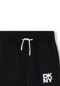 Pantalons de jogging noirs avec une taille élastique à cordon, des détails d'accentuation blancs et un logo blanc avec "DK NY" sur le côté gauche. Texture douce.