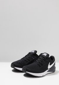 Scarpe sportive nere con tomaia in rete, logo Nike swoosh bianco, suola intermedia bianca in contrasto, suola testurizzata e chiusura con lacci tradizionale.