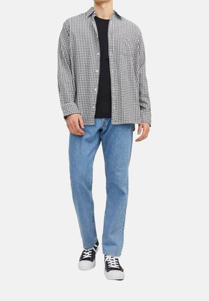 Zwart-wit geruite shirt over een zwart t-shirt, gecombineerd met lichtblauwe jeans en zwarte sneakers met witte veters.