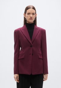 Bourgondisch colbert met een getailleerde pasvorm, een enkelrijig ontwerp, ingetogen revers, twee voorzakken en twee knopen. Gladde weefseltextuur.