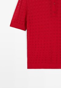 Red short-sleeve knit polo shirt with textured diamond pattern and three buttons on the front placket, shown from the chest down.