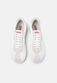White sneakers with a smooth leather upper and suede accents. Features flat laces, a textured sole, and a red "CAMPER" logo on the tongue.