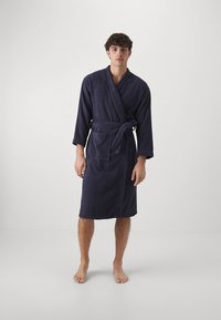 Robe de banho de tecido felpudo azul-marinho com mangas compridas, design envolvente, detalhe de cinto e bolsos frontais; textura macia e comprimento até ao joelho.