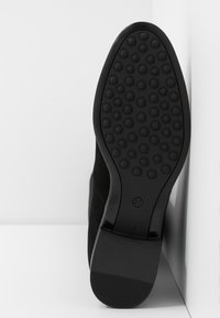 Bottine en suède noir avec une semelle en caoutchouc texturé, dotée d'un bout rond et d'un petit talon carré. Taille 37 marquée sur la semelle.