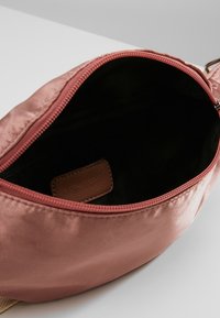 Kleine open dusty pink stoffen zak met een zichtbaar bruin leren label aan de binnenkant en een rits langs de bovenrand.