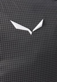 Un tissu noir avec un motif en grille présente un accent blanc angulaire sur le dessus, ajoutant un détail visuel distinct au design global.