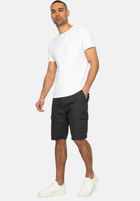 Camiseta blanca de manga corta combinada con pantalones cortos cargo negros que tienen bolsillos laterales, llevados con zapatillas blancas. Un atuendo simple y casual.