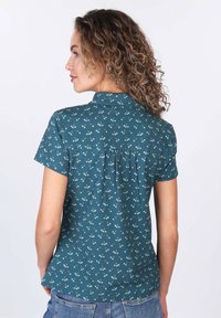 Teal short-sleeve blouse featuring a floral pattern, collar, and pleat detail on the back, made from lightweight fabric.