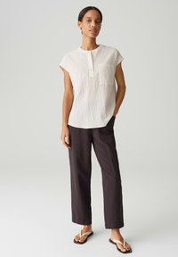 Blusa leggera di cotone con maniche corte, righe verticali e scollatura con bottoni. Abbinata a pantaloni scuri e larghi e ciabatte.