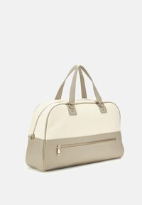 Borsa da viaggio in tela e pelle, di colore crema e beige, con doppi manici superiori, una tasca frontale con zip e una superficie liscia.